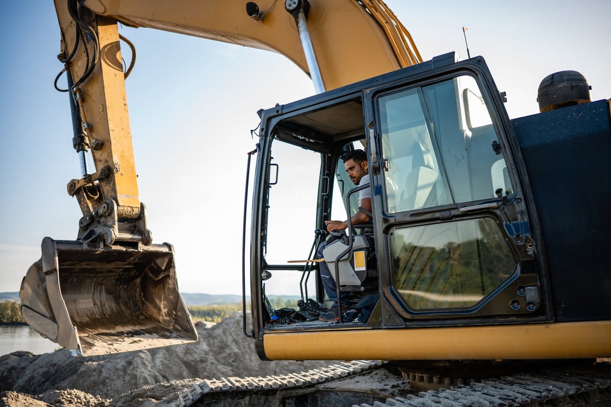 Construction worker operating a large excavator at a busy construction site