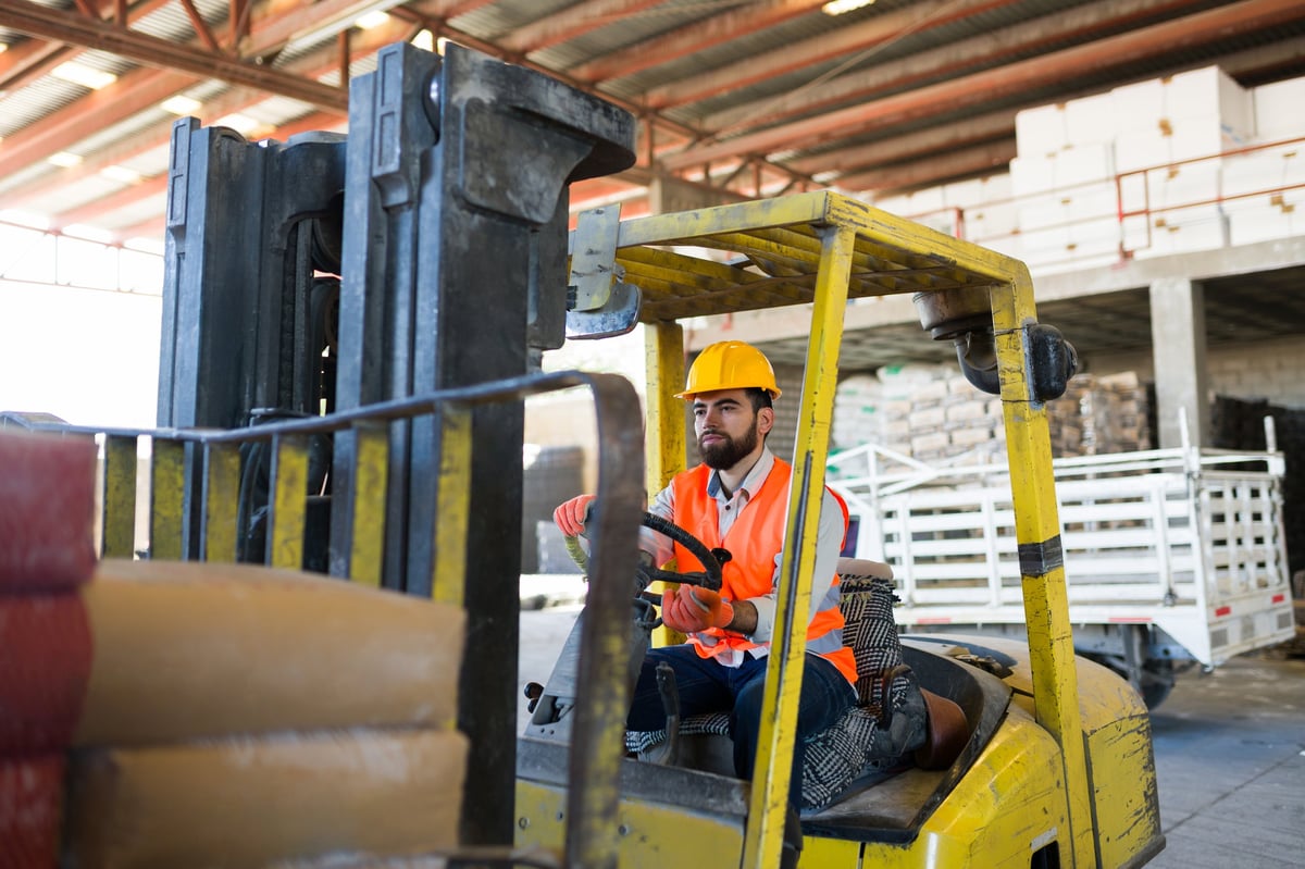 Worker operating forklift in industrial warehouse at construction supply store, managing inventory and logistics operations