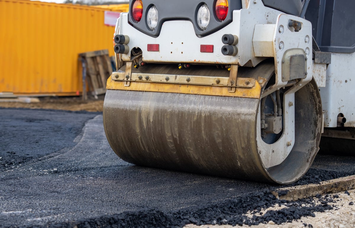 A road roller is working on a new road, flattening asphalt